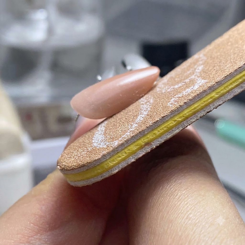 A nail file buffer shaping and smoothing the three sides of a finished gel nail.