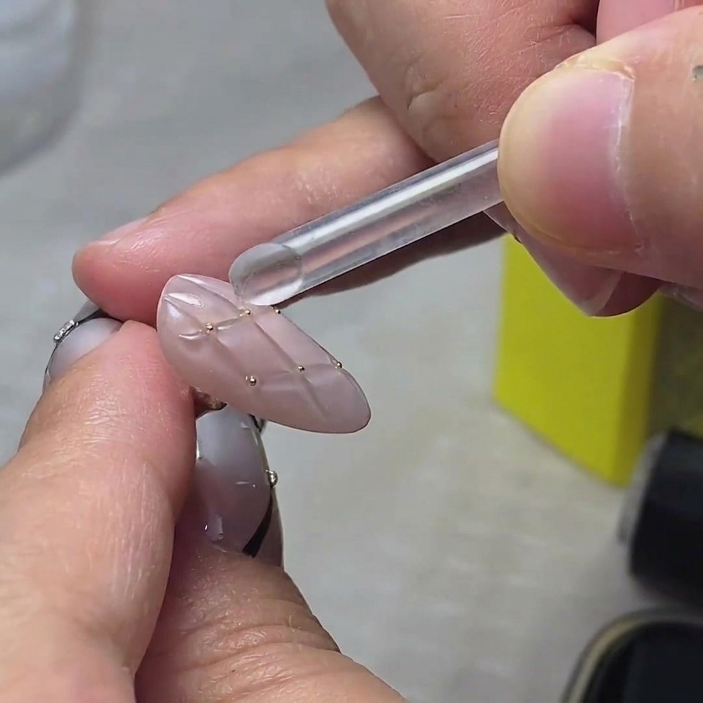 A close-up view of golden glitter flakes being applied onto the tip of a nail.
