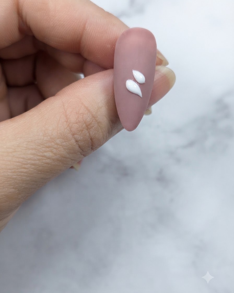 A close-up of a pinkish-nude nail showing two distinct white teardrop-shaped petal strokes applied near the center.