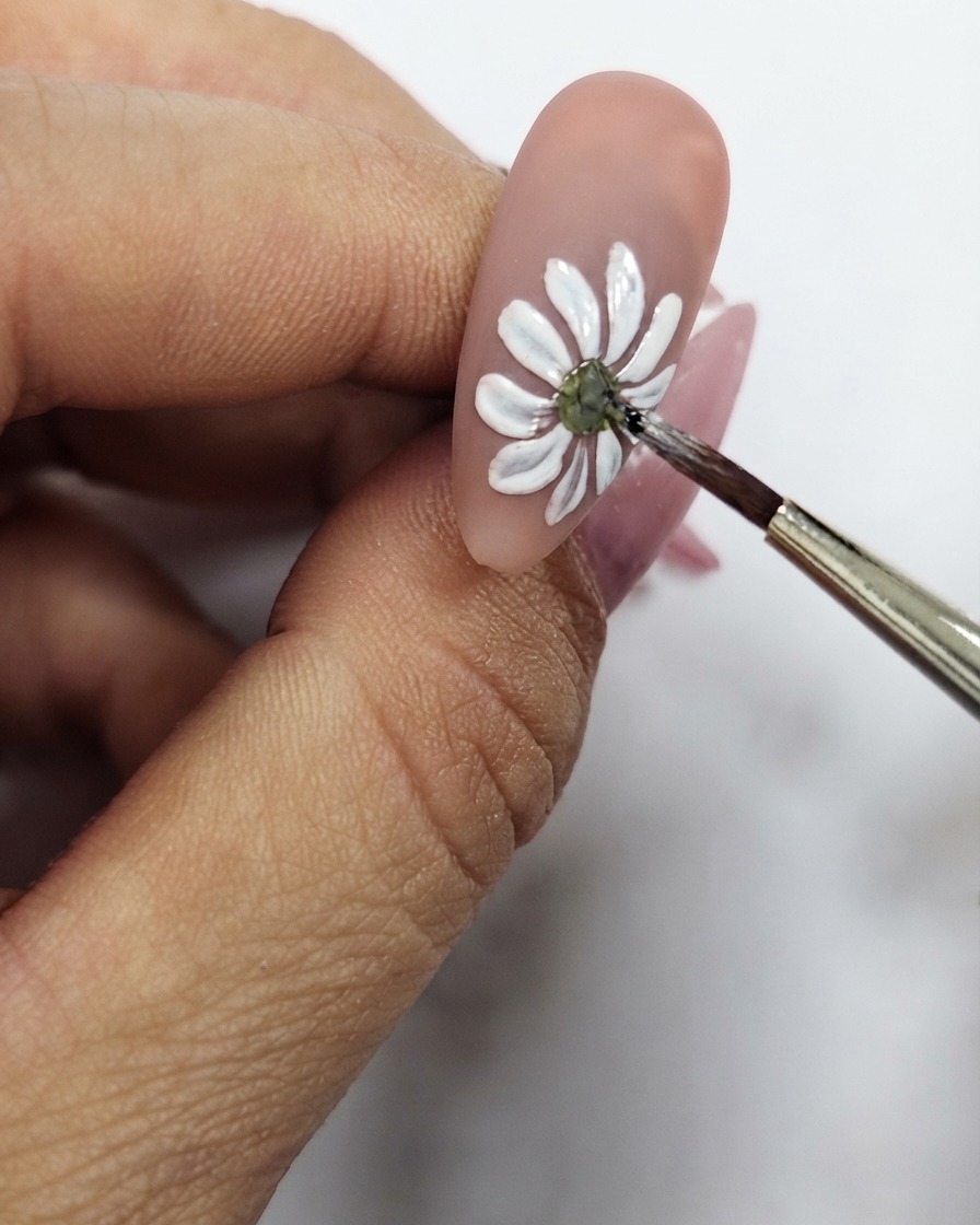 A close-up of a fine brush refining the yellow center dot of the white daisy nail art.