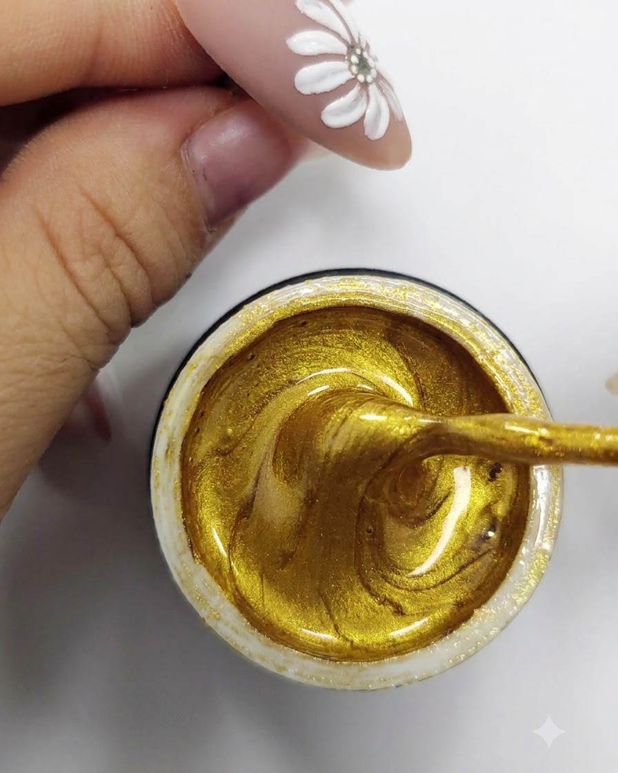 A fine liner brush scooping and loading vibrant gold gel polish from inside an open container.