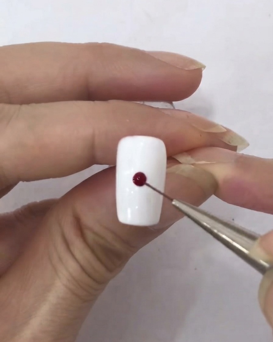 A fine liner brush picking up a tiny droplet of dark red gel polish.