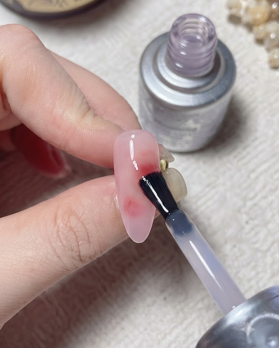 A brush applying a top layer over a cured nail design with a silver bottle in the background.