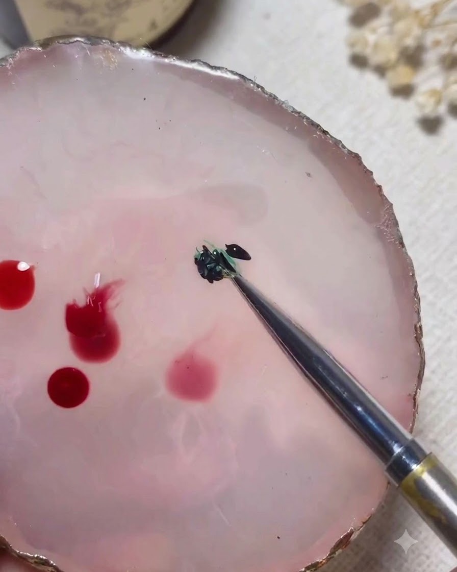 A mixing tool blending green and black gel colors together on a pink marble palette.
