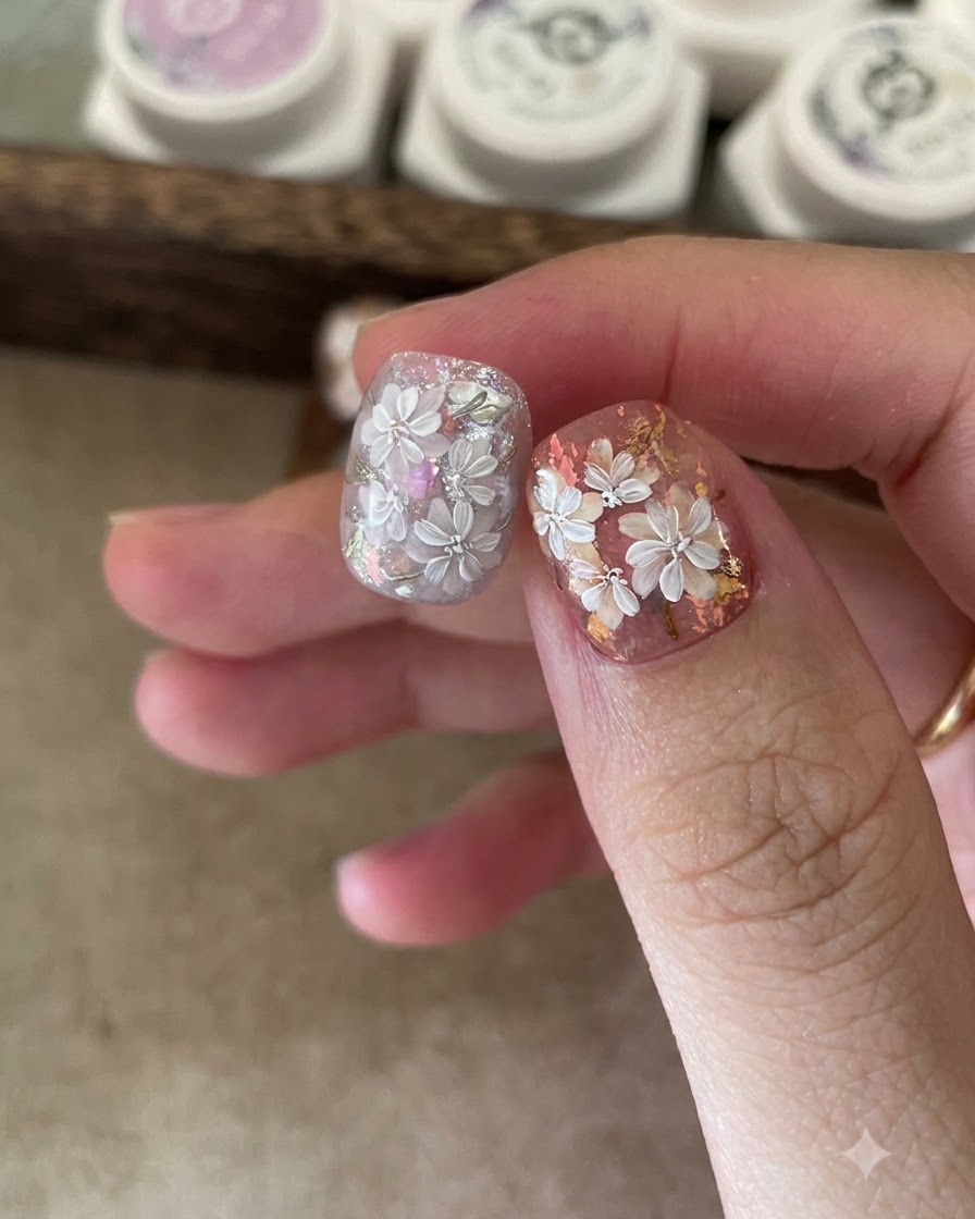 A close-up of tweezers placing iridescent foil flakes onto a tacky gel base on a fingernail.