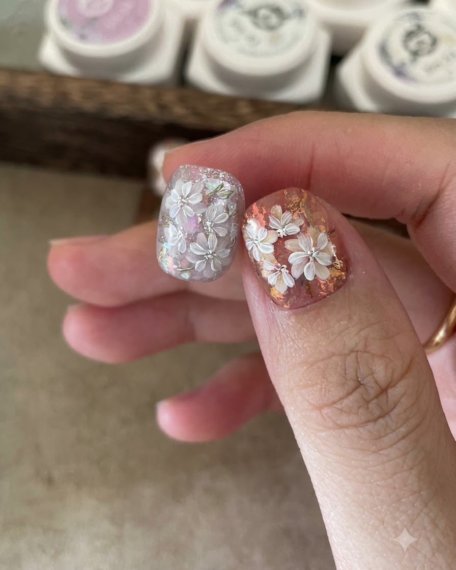 A fine liner brush drawing white five-petal flower outlines on a decorated nail.