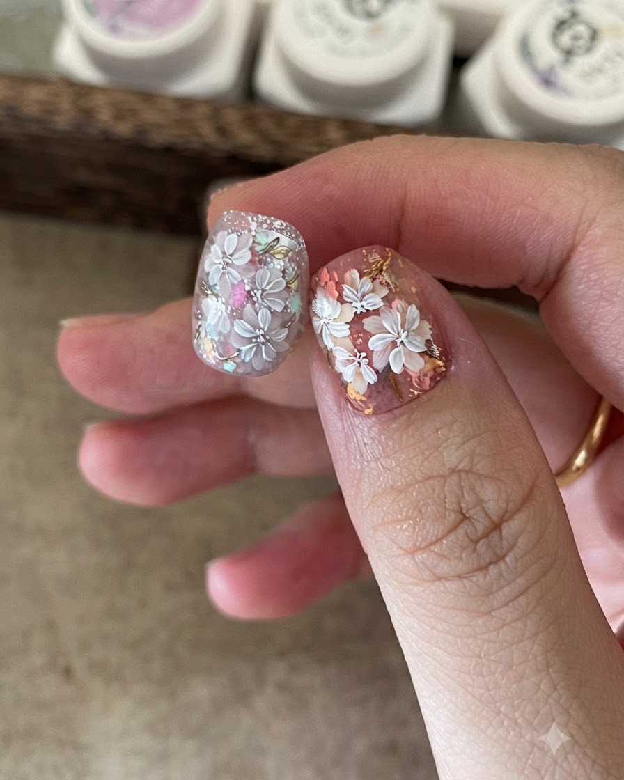 A close-up of a nail artist using a small sponge to apply colored gel to the center of white floral nail art.