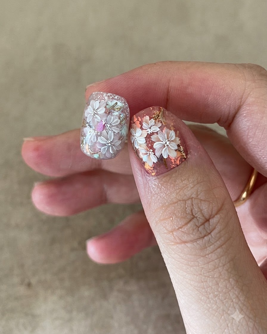 A nail brush applying a clear top coat over intricate floral and gold foil nail art.