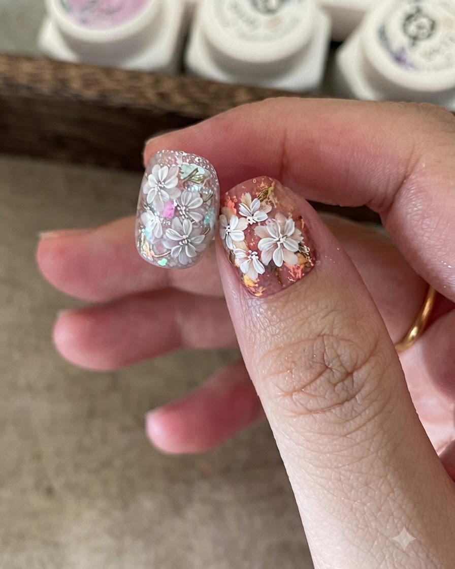 A fine nail art brush adding detailed white petals over a pre-painted floral nail design.