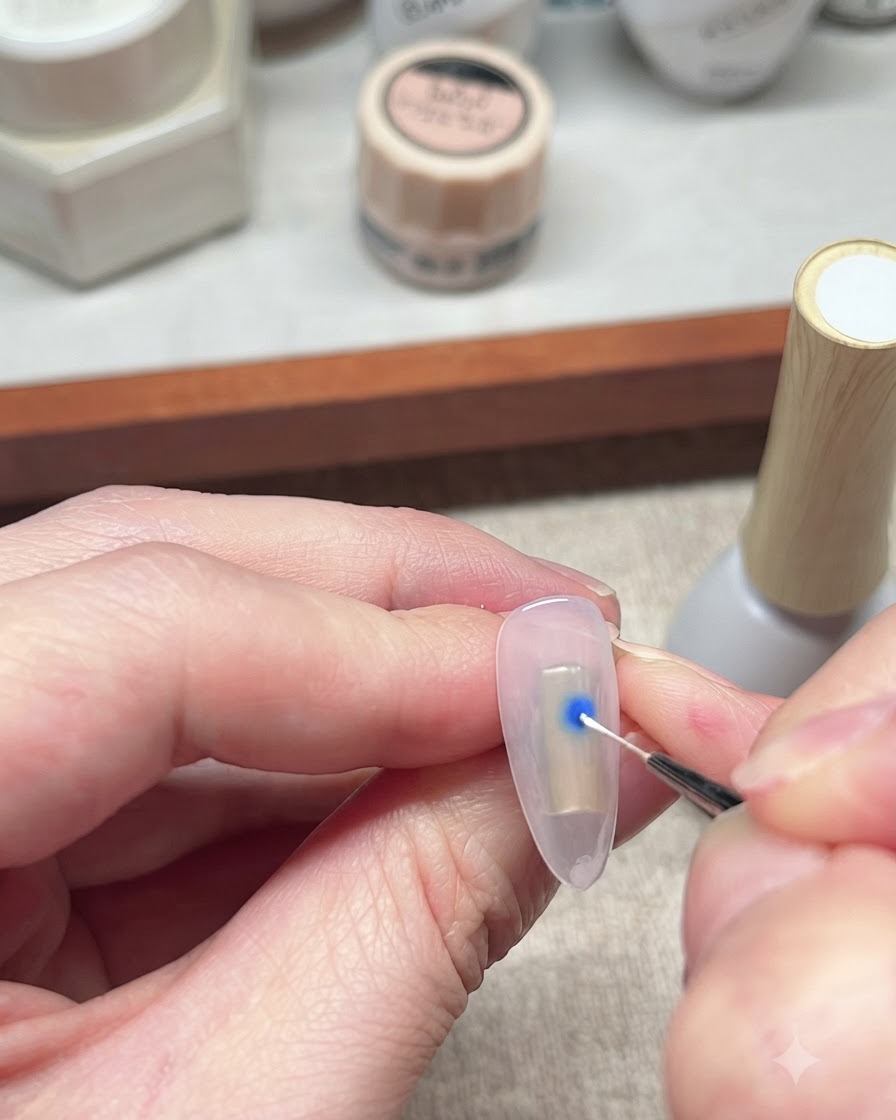 A fine liner brush interacting with a blue dot of gel polish on a nail to start the blooming effect.