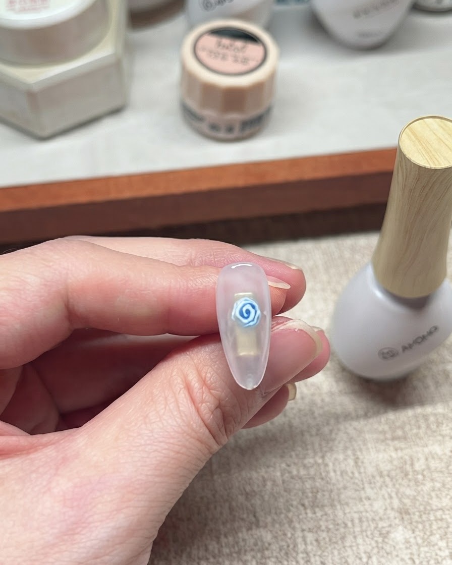A close-up of a finished blue rose gel nail design resting next to a white bottle of nail product.