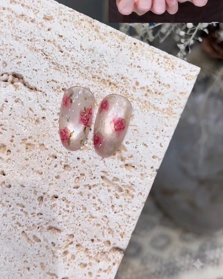 A close-up of a hand using a fine liner brush to paint delicate outlines on a milky translucent nail.