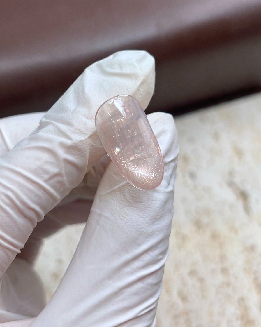 A gloved hand holding a magnetic wand over a shimmering cat-eye gel nail to create a pearl effect.