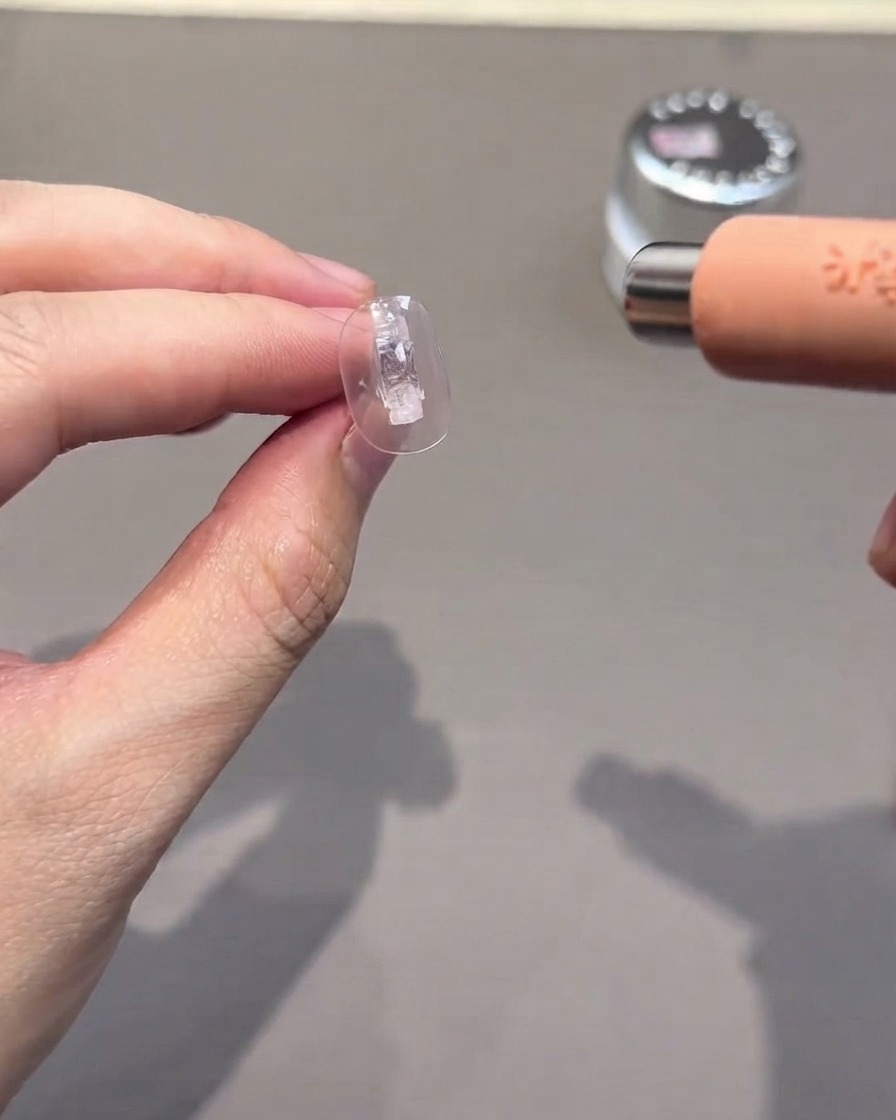 A clear nail tip being cured under a small portable UV/LED lamp.