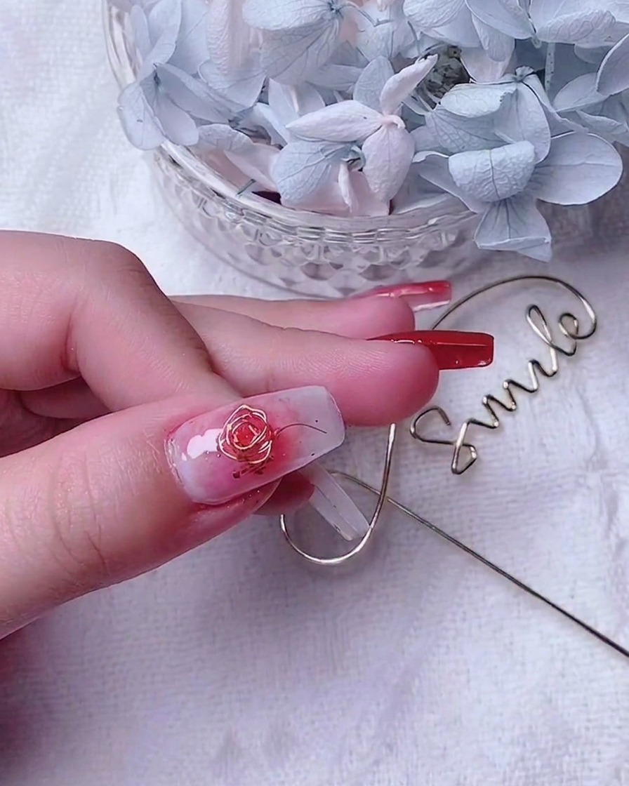 A close-up shot of a decorated thumb nail featuring a gold wire rose and small accent wires along the edge.