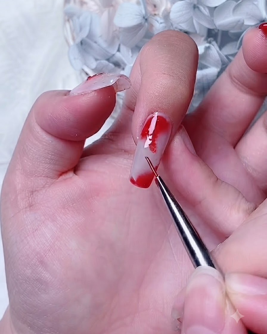 A detail brush applying red gel onto a blooming gel layer at the corner of an index nail.