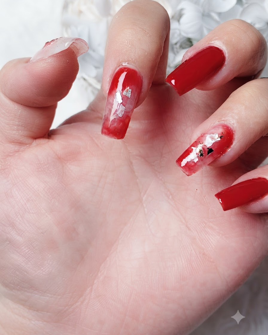 Close-up view of small leaf-shaped gold foil pieces being placed into a diffused red blooming gel area on a fingernail.
