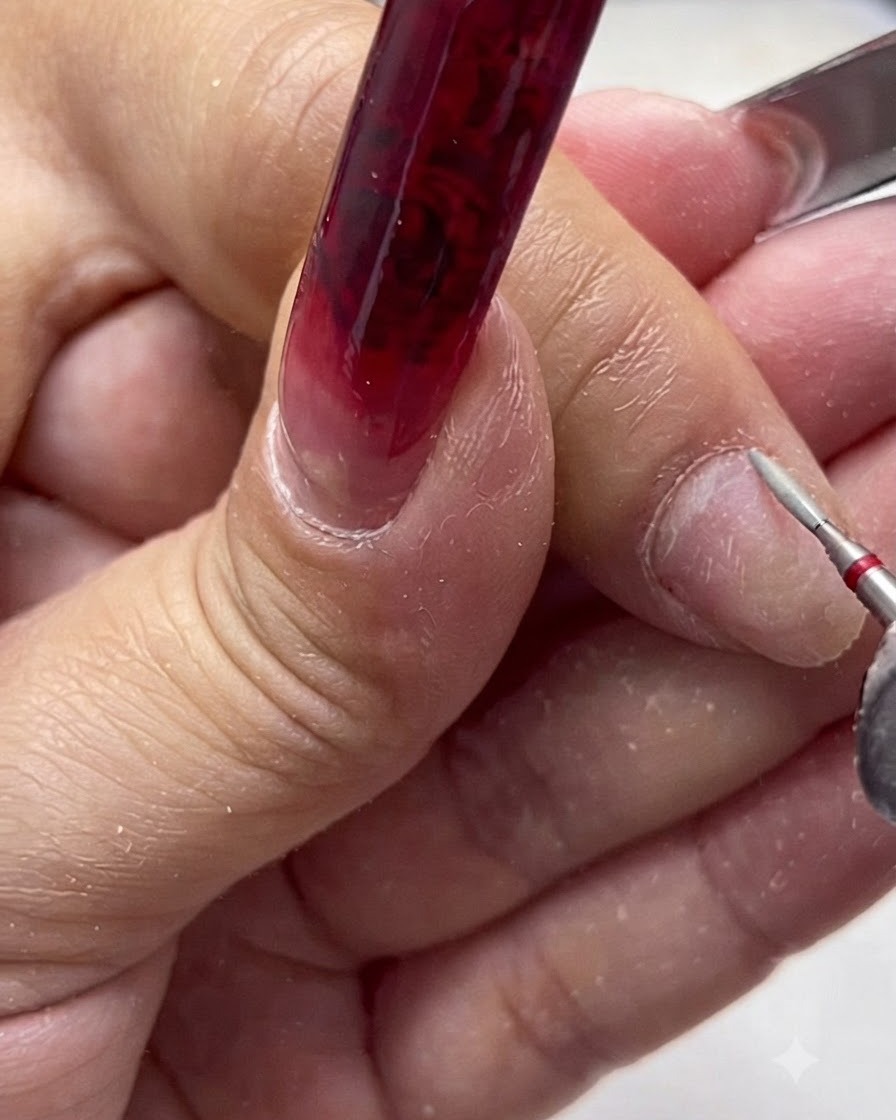 An electric nail file with a ceramic safety bit detailing the cuticle area of a natural fingernail.