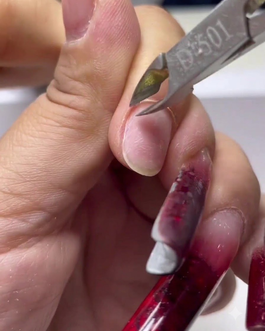 A close-up of sharp metal cuticle nippers trimming away dead skin from the base of the fingernail.