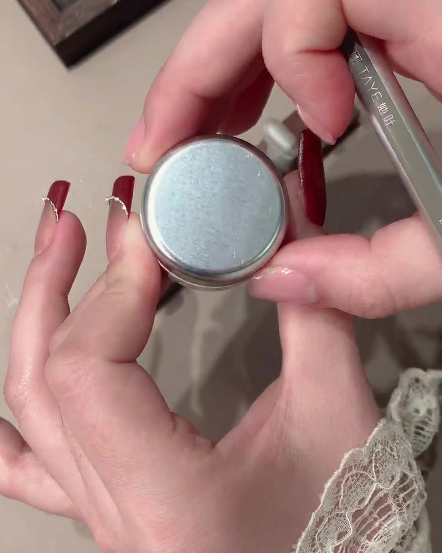 A brush applying red velvet gel onto a clear nail tip.