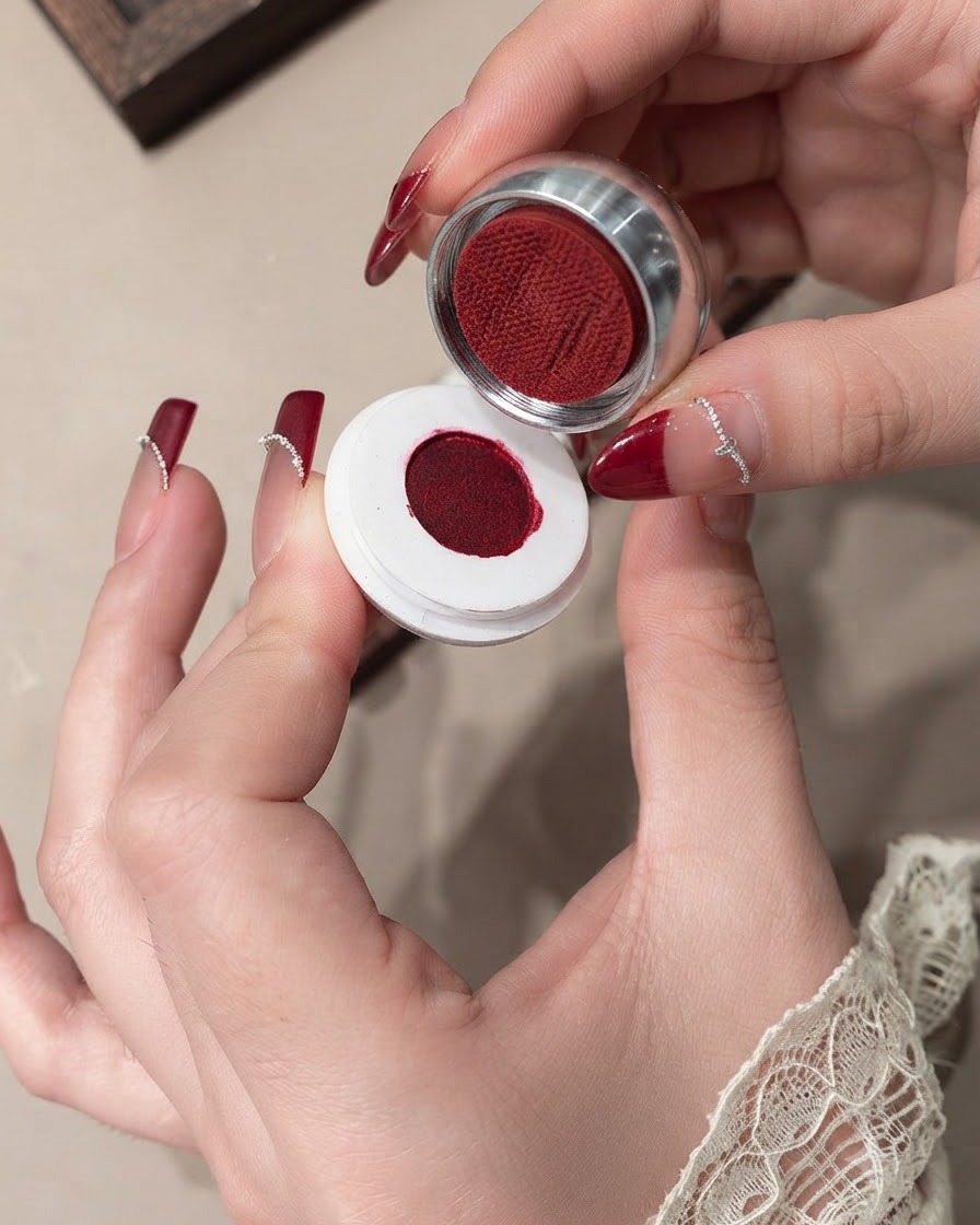 A close-up of a brush smoothing red velvet gel on a nail.