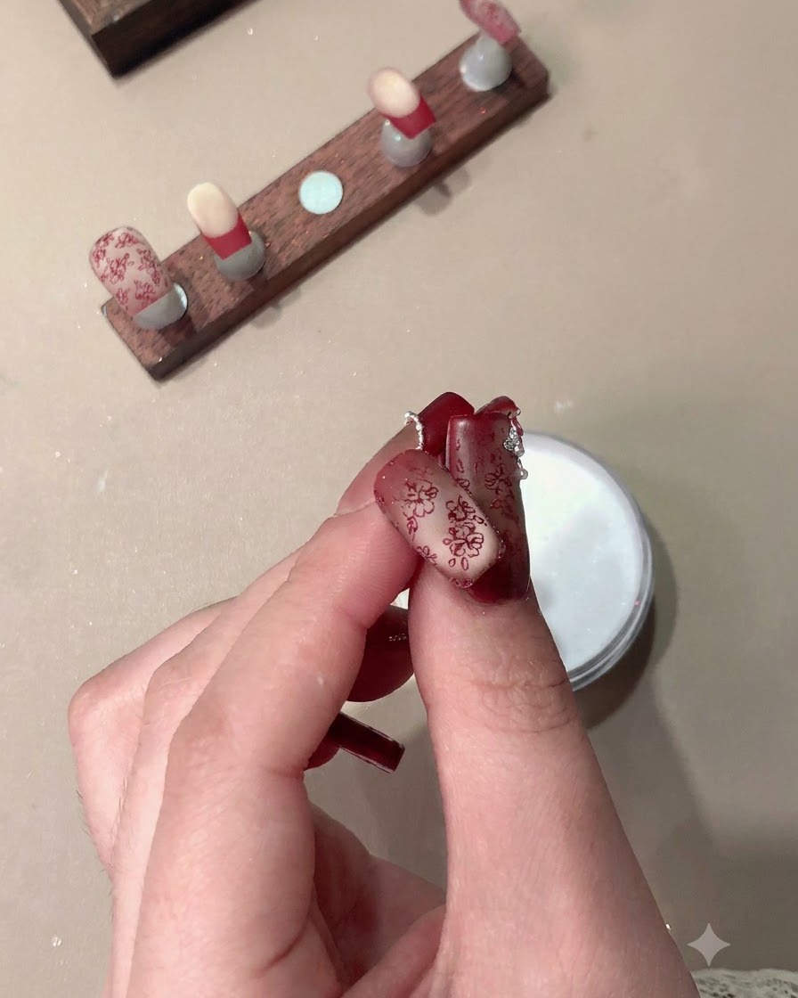 A hand holding finished press-on nails featuring stamped red patterns and French tips.