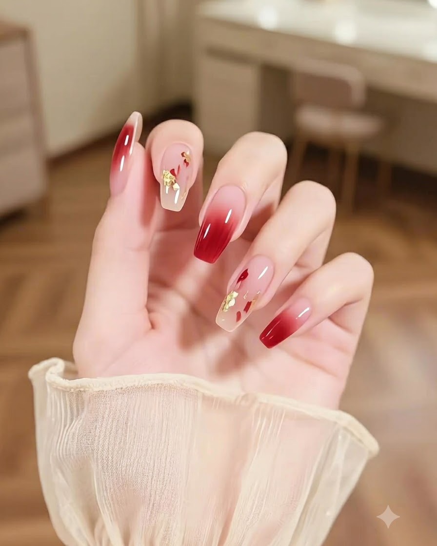 A close-up of a hand featuring an accent nail with abstract multicolored brushstrokes and gold sparkles next to burgundy ombre nails.