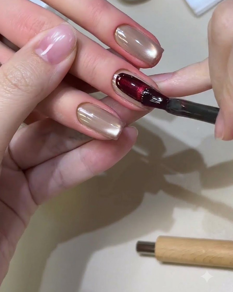 A nail brush applying a rich red cat-eye gel onto a square-shaped nail.