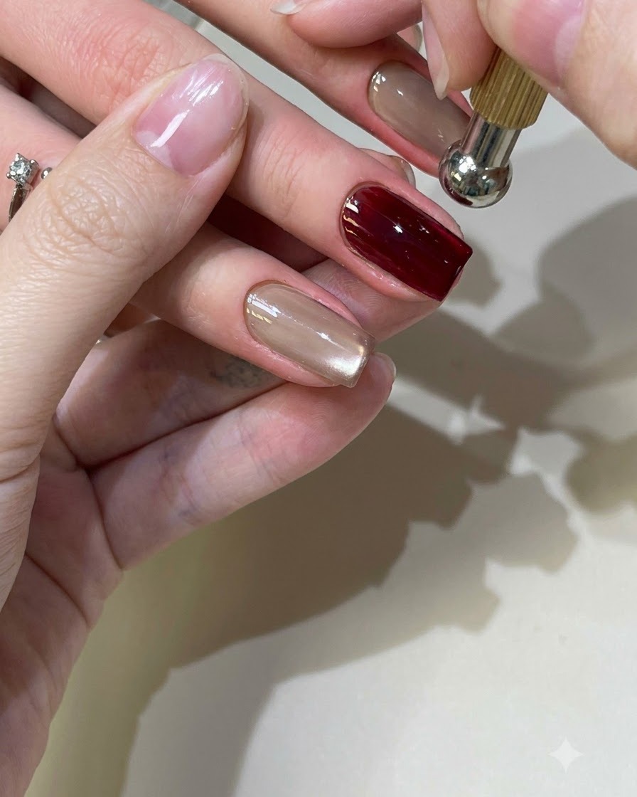 A spherical magnetic tool hovering over a red cat-eye gel nail to shape the light reflection.