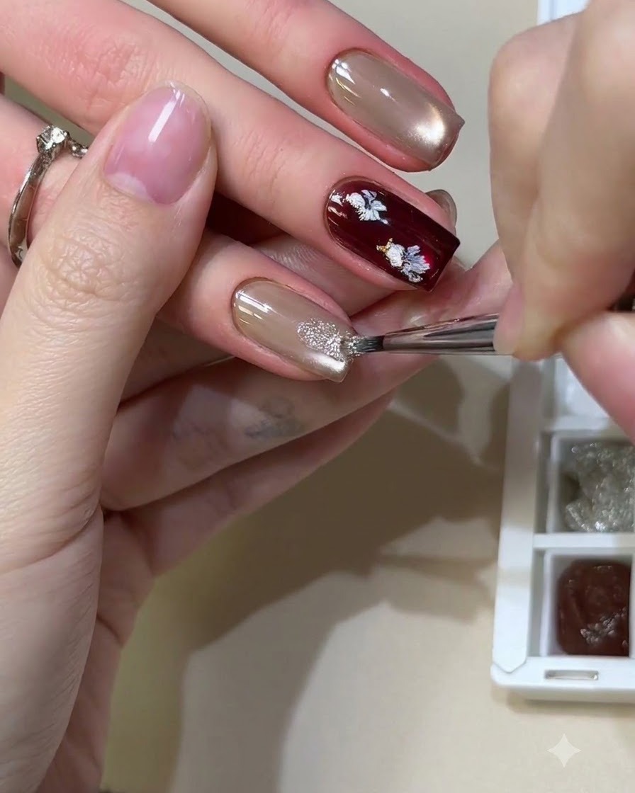 A fine brush dabbing shiny reflective glitter materials onto a neutral cat-eye gel nail.