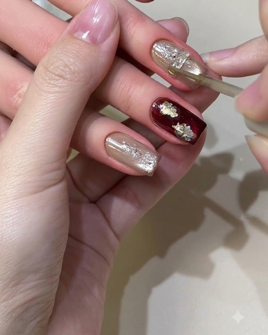 A fine brush meticulously applying gold metallic liquid details onto a textured, shimmering nail design.