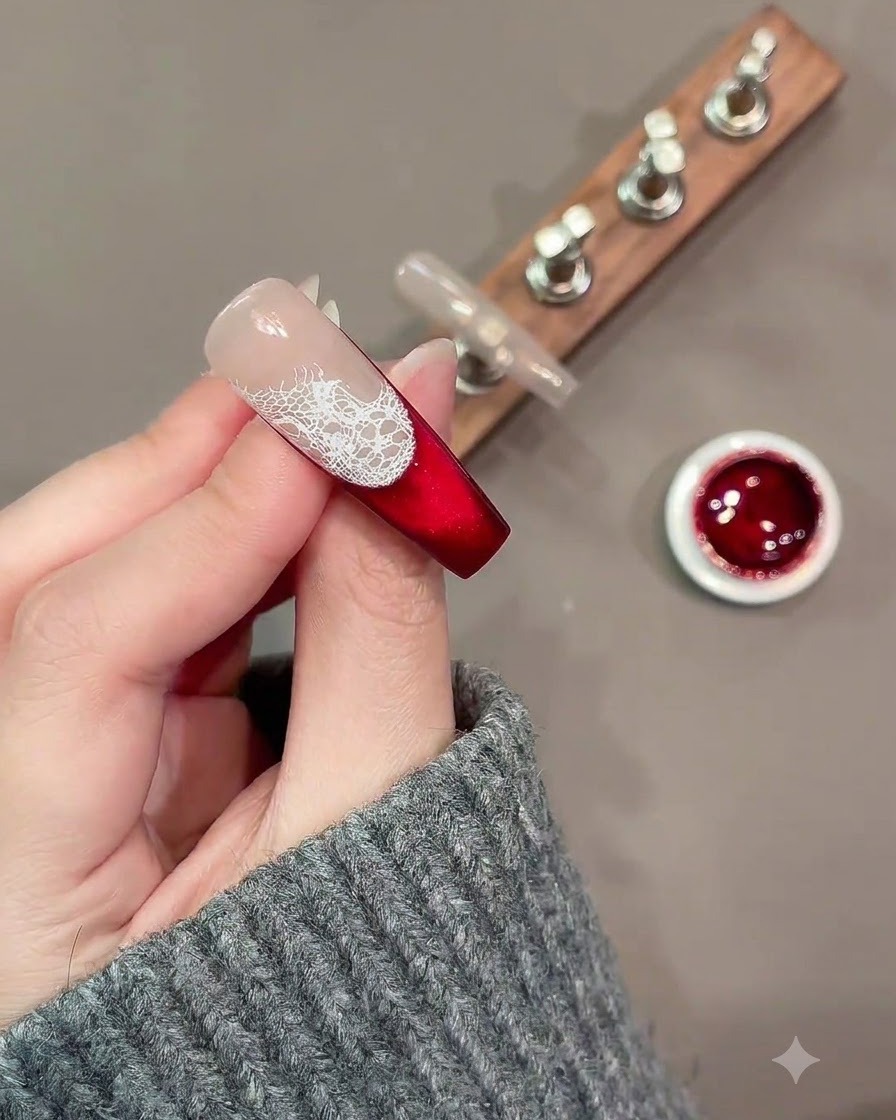 A fine nail art brush painting loose white rose outlines over a lace pattern on a red and nude nail.
