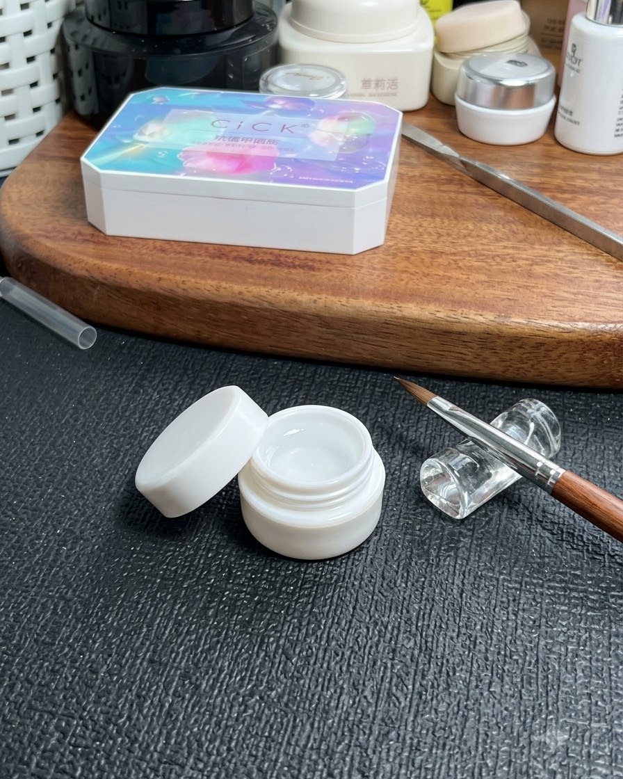 A jar of clear base gel placed on a table next to a fine nail art brush and a cosmetic storage box.