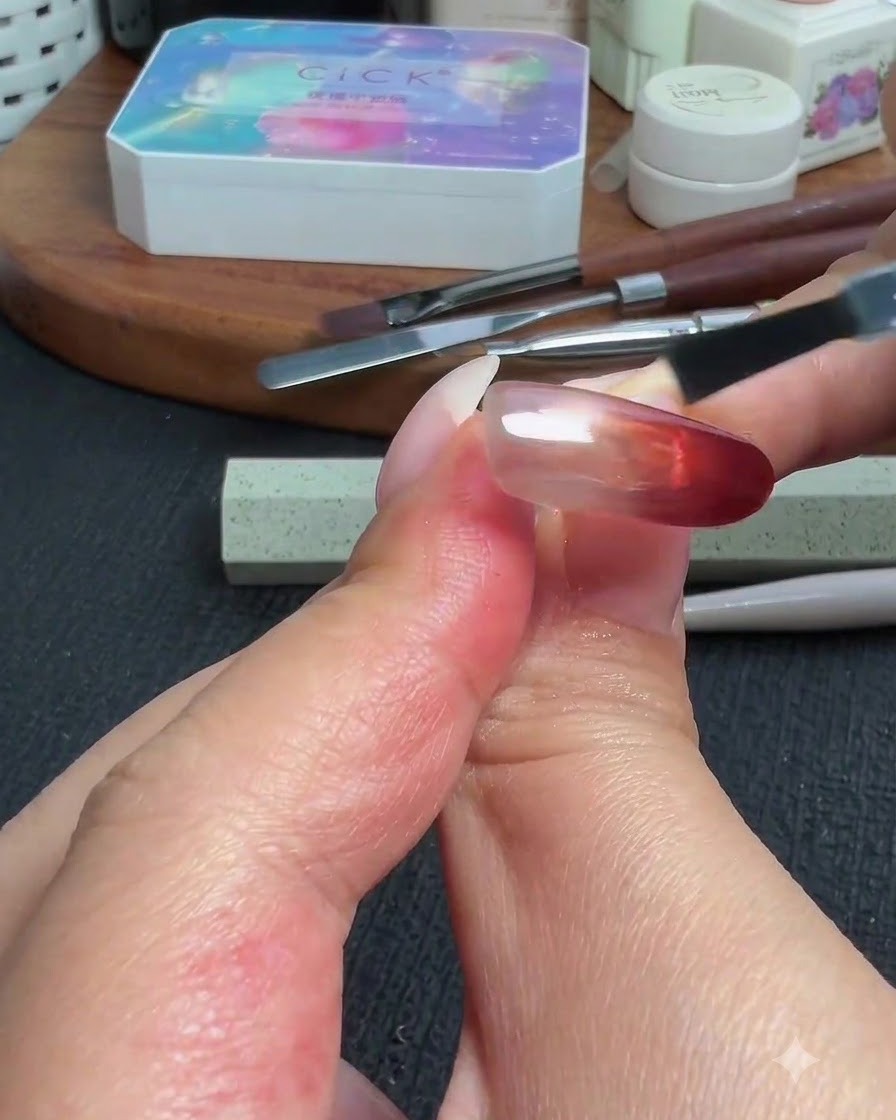 A brush applying a glossy top coat over the completed red cat-eye and powder gradient nail.