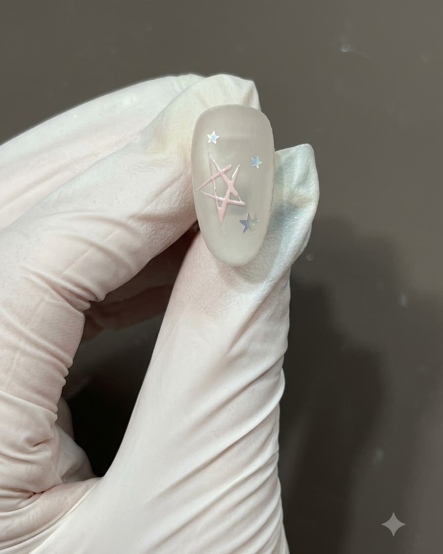 A fine nail art brush filling the center of a hand-drawn star outline with light pink gel polish on a matte nail.
