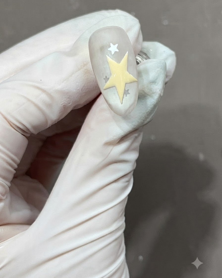 A freshly drawn and filled yellow five-pointed star next to other stars on a matte nail.