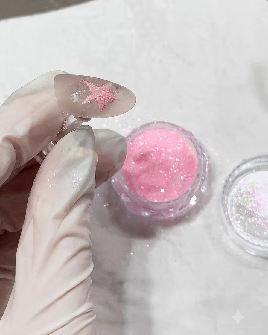 A nail covered in textured pink diamond powder right before being cured under a lamp.