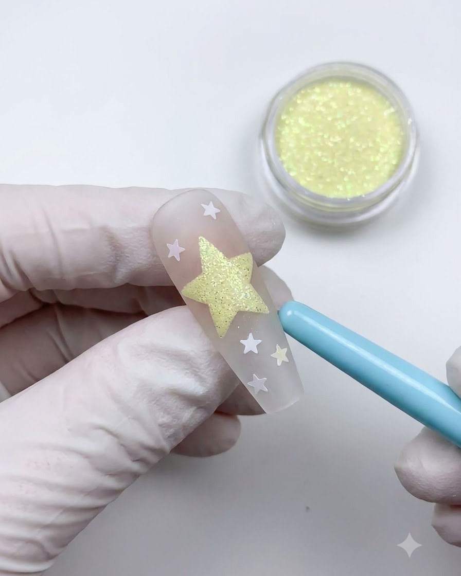 A soft blue dusting brush sweeping away loose powder to reveal a textured star nail art design.