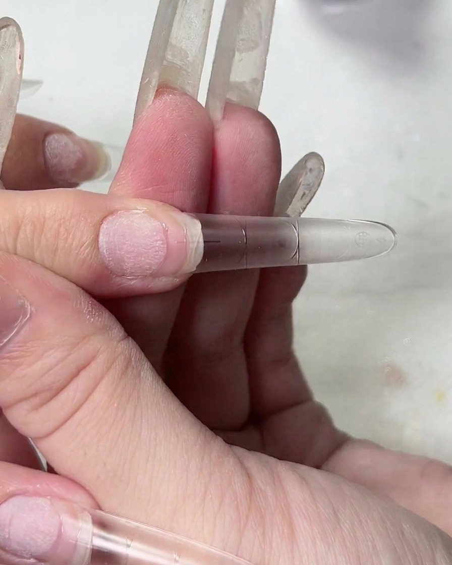 A close-up of a hand lifting a nail tip, showing the stringy texture of the clear adhesive gel.