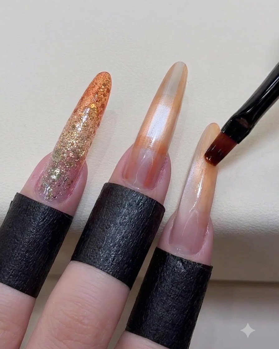 A brush softly blending the edges of orange color blocks on a long manicured nail.