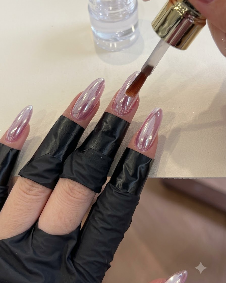 A brush applying clear top coat over glossy chrome-finished nails.