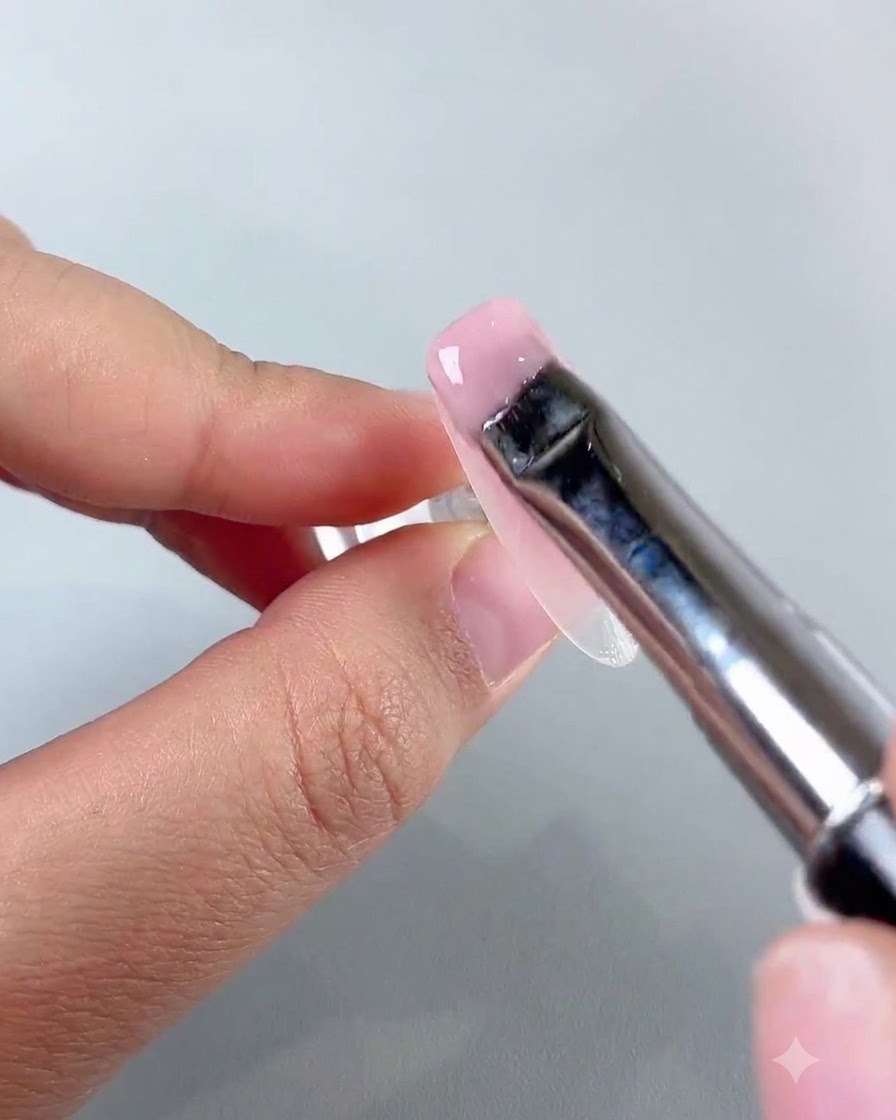 A flat nail art brush spreading a smooth layer of light pink jade base gel over the nail surface.