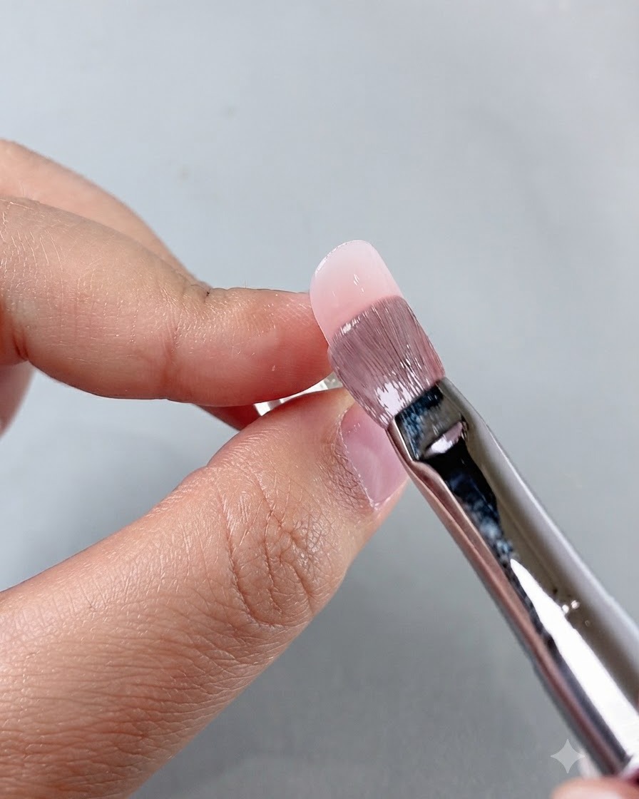 A manicure brush smoothing product near the cuticle area while working on the nail application.