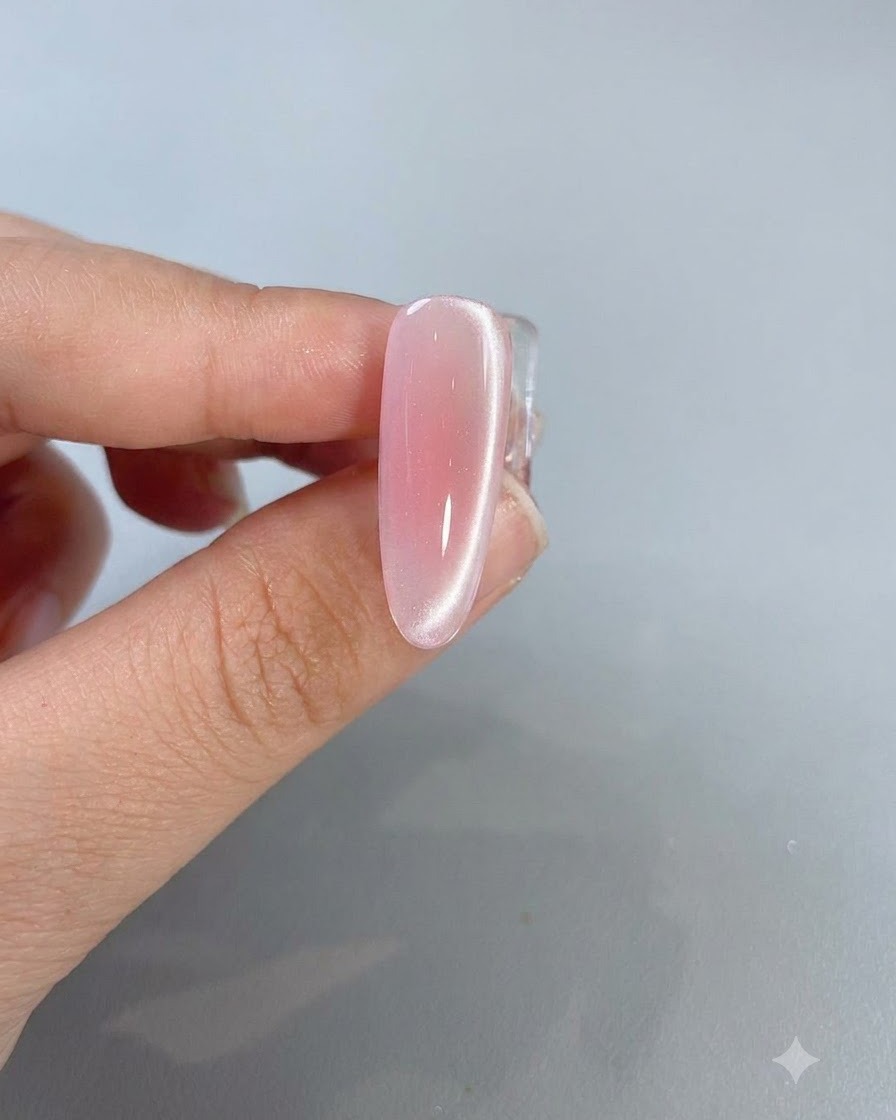 A close-up of a completed pink cat-eye nail showing a bright light reflection line running down the side.