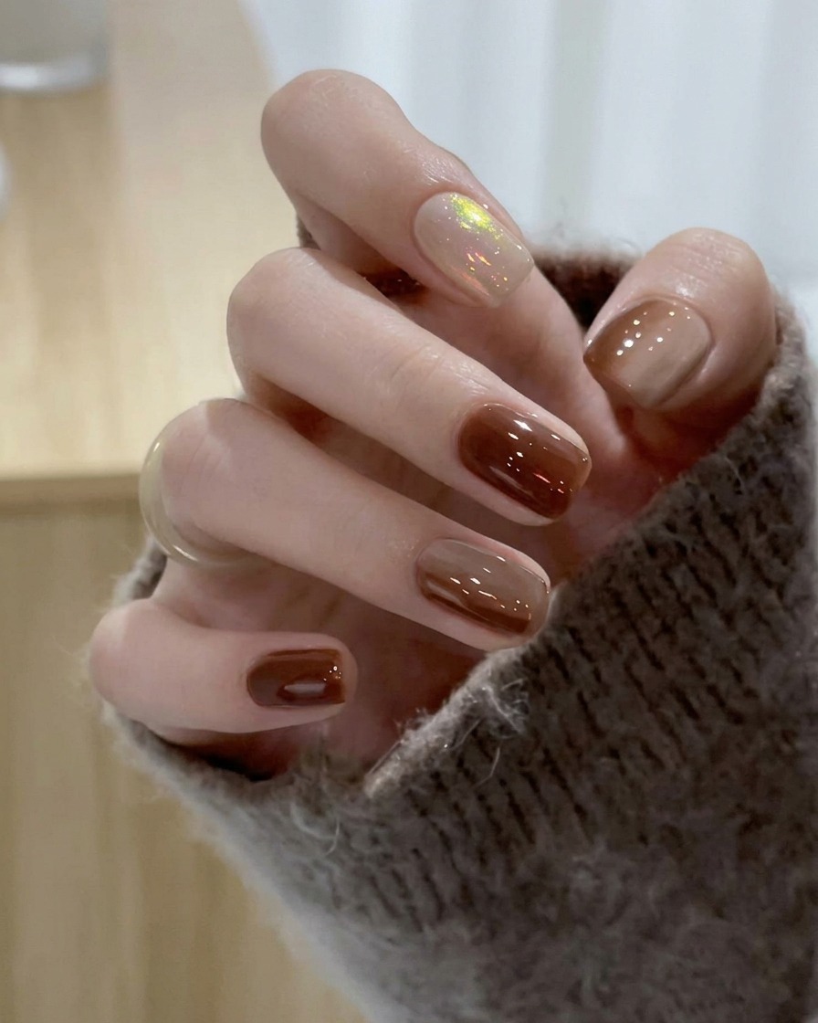 A brush gliding translucent nude gel polish over the middle fingernail.