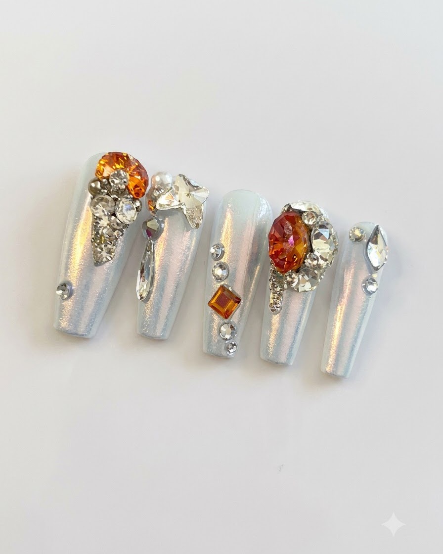 A close-up macro photograph showing fine silver beads, small rhinestones, and butterfly charms clustered on press-on nails.