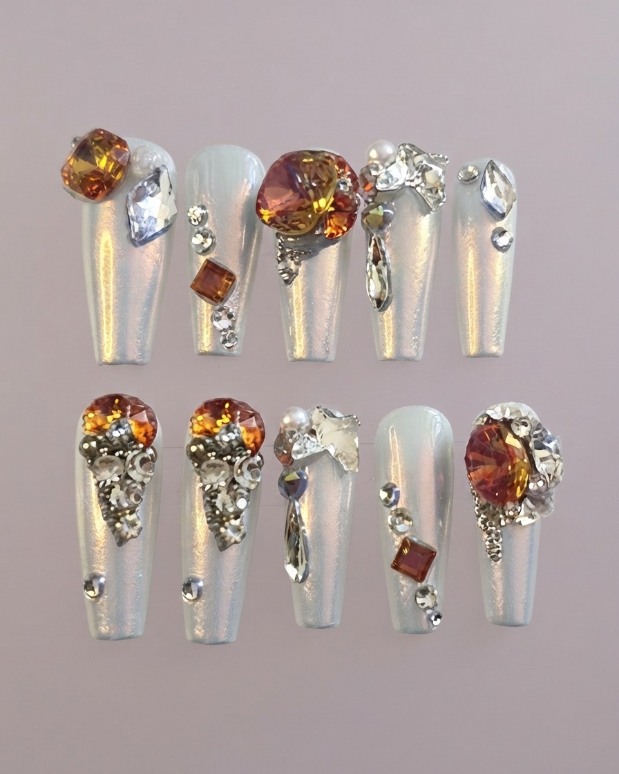 A detailed shot of a statement thumb press-on nail featuring a prominent amber gemstone surrounded by clear crystals.