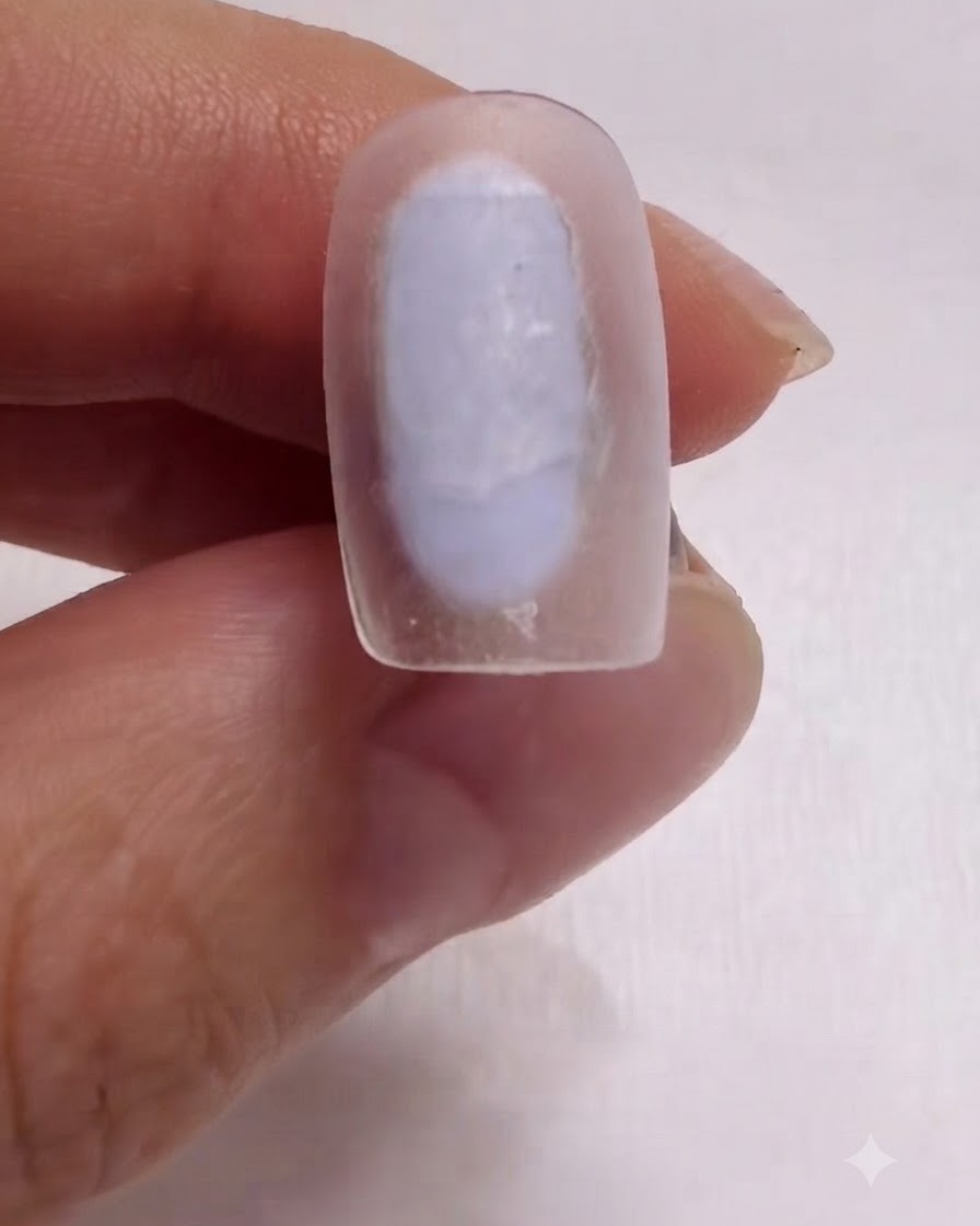 A brush carefully applying a milky white base coat onto a nail surface.
