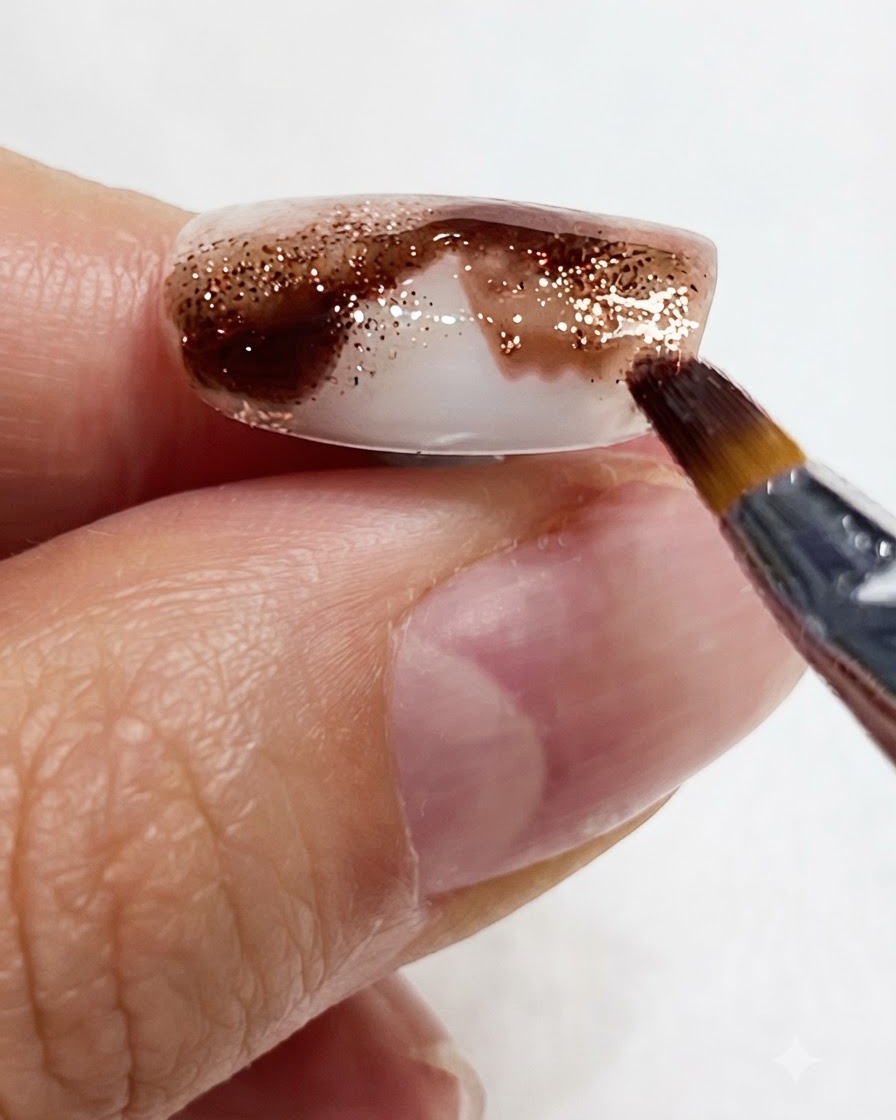 A close-up shot showing a fine brush drawing amber watercolor pigment downward along the nail.