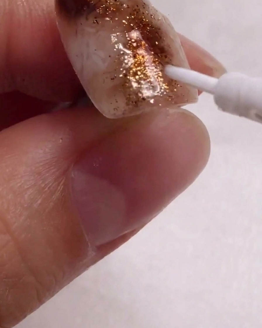 A close-up view of a fine liner brush applying white details onto the textured nail design.